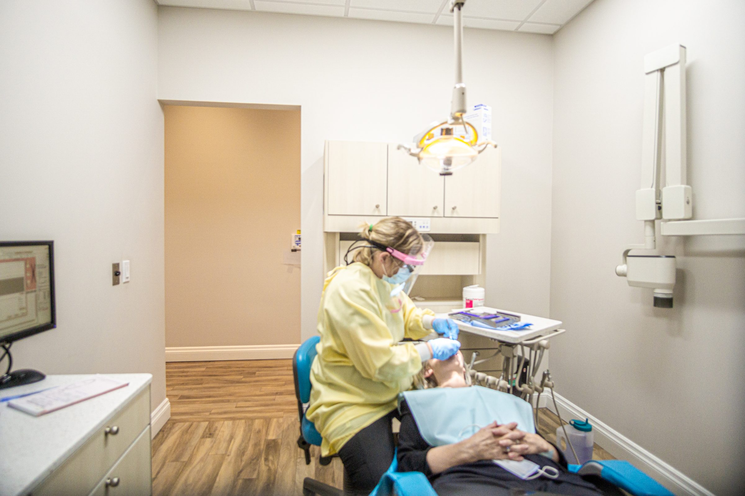A dental professional in protective gear examines a person in a modern, well-equipped dental clinic with tools and equipment visible.