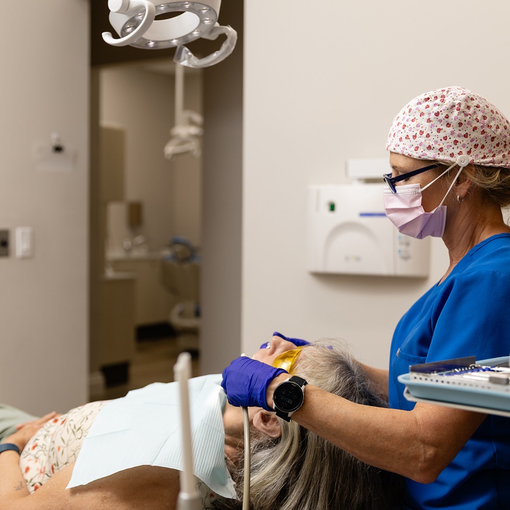 A dental professional attends to a patient, wearing gloves and a mask, in a modern dental clinic setting.