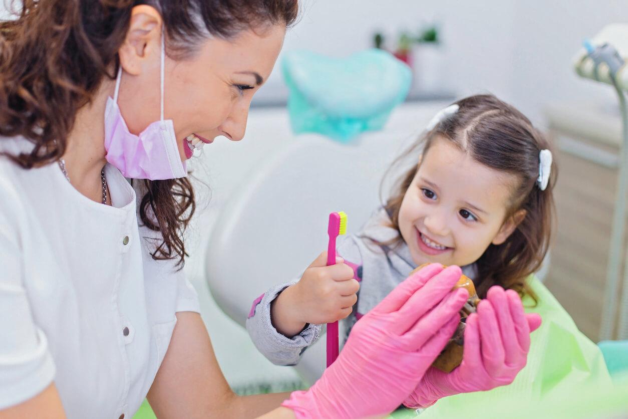 A person and child engage in dental hygiene activity at a clinic, with both smiling. The child holds a bright pink toothbrush.