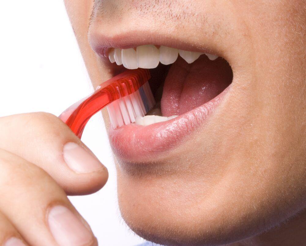 Close-up of a person brushing their teeth with a red toothbrush. The focus is on the open mouth and white teeth.