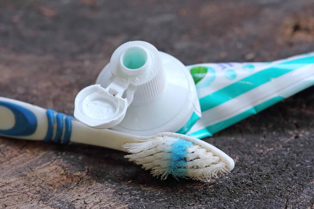 A close-up of a toothbrush with blue bristles and a partially squeezed toothpaste tube on a wooden surface.