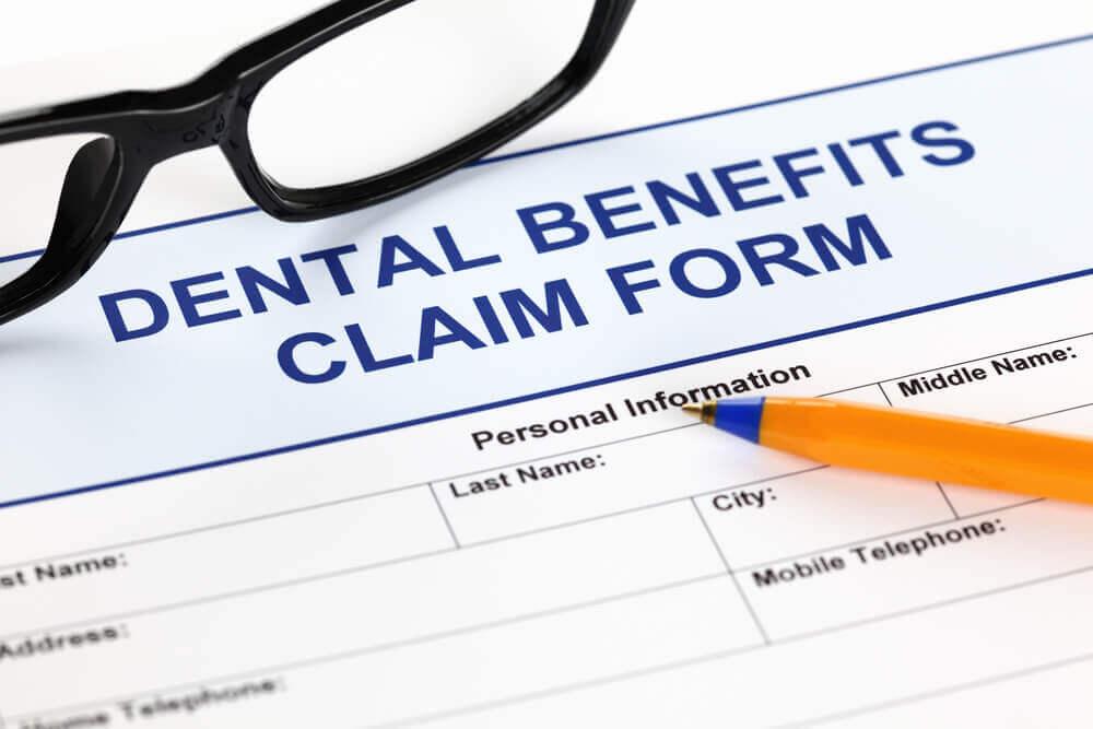 A dental benefits claim form alongside eyeglasses and an orange pen, ready for completion with personal information details.