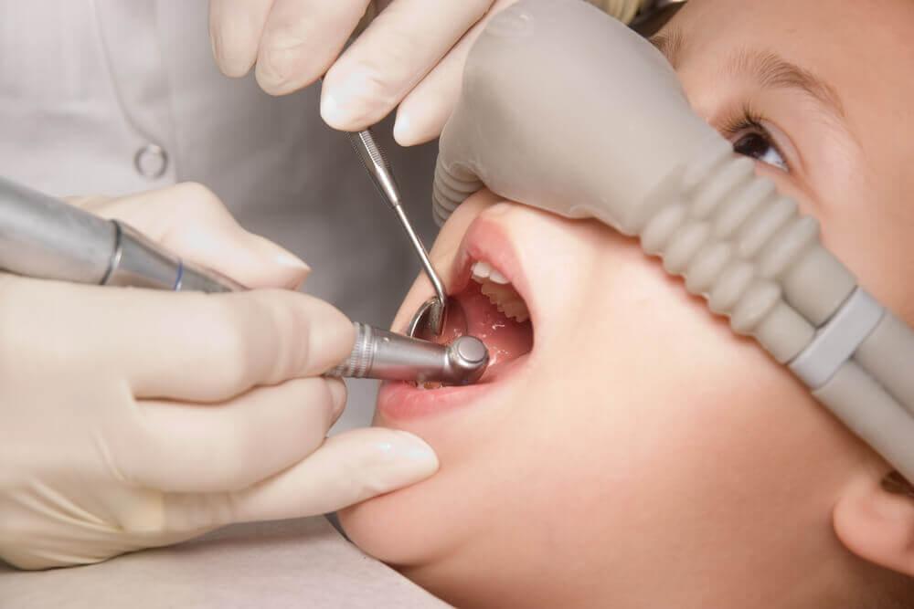 A dental procedure on a child using dental tools and numbing equipment, with a person wearing gloves working carefully on their teeth.