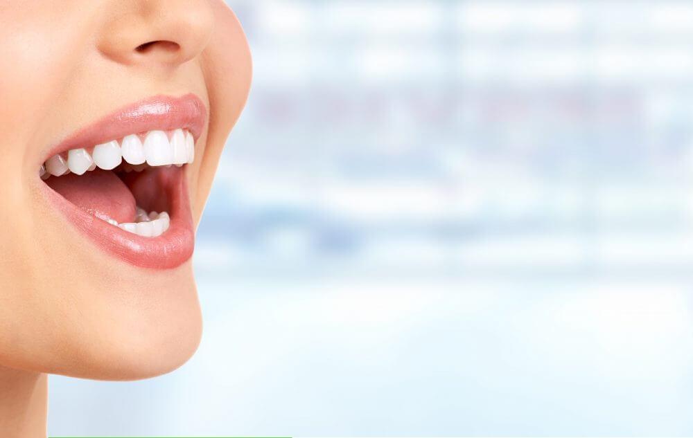 A person with a bright smile is shown in a close-up, displaying clean, white teeth. The background is blurred.