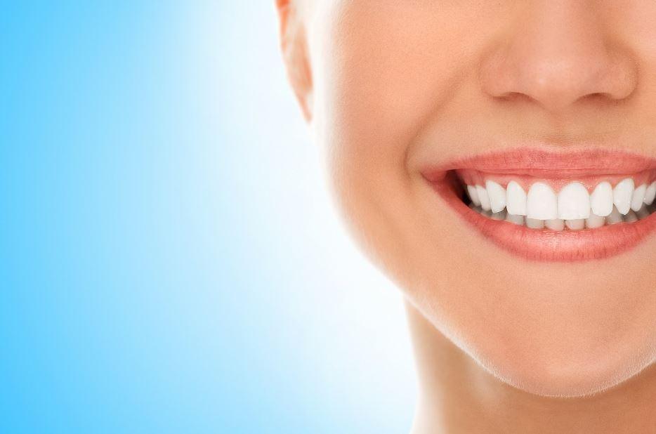 A close-up of a smiling person with white teeth against a smooth blue gradient background, showcasing a healthy dental aesthetic.