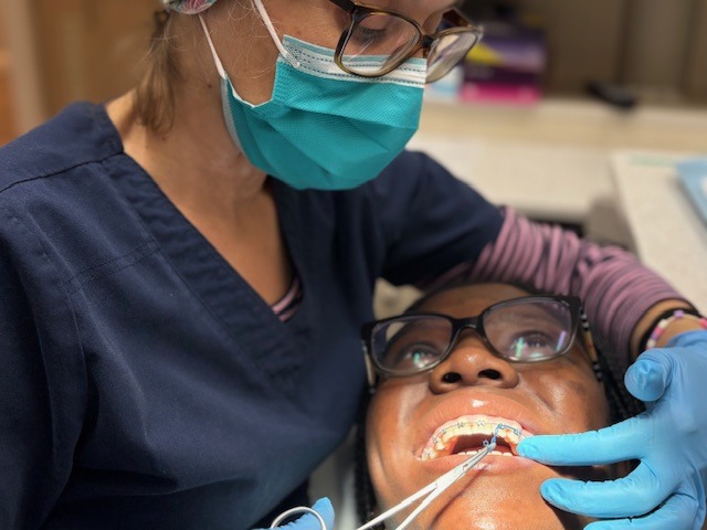 A person wearing scrubs and a mask tends to another person's teeth in a dental setting. Instruments are being used during the procedure.