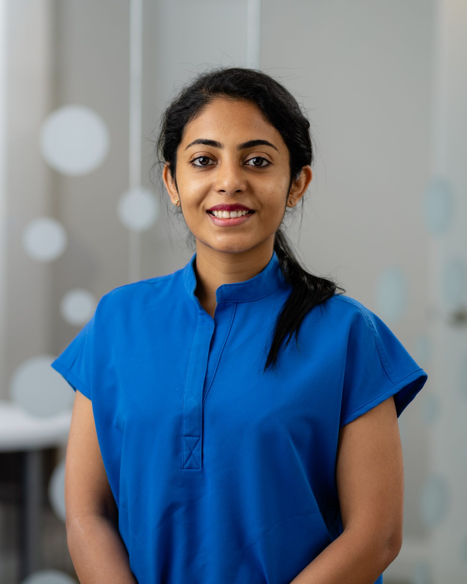 A person wearing a blue shirt smiles in a room with blurred circular decor on the glass background. No landmarks or buildings visible.