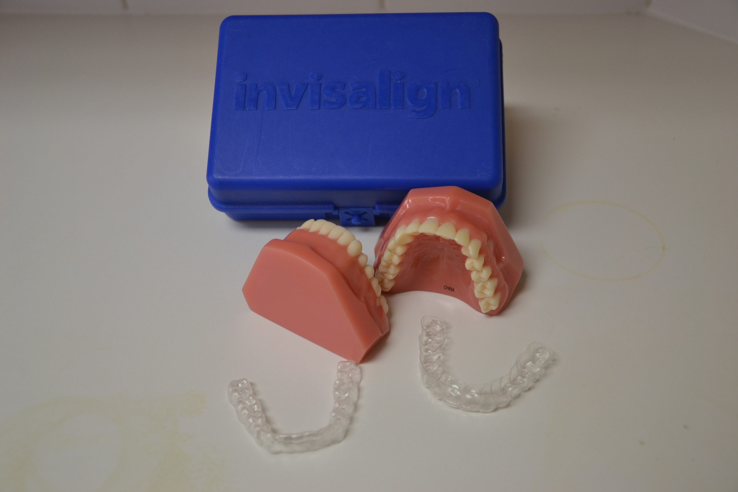 Blue Invisalign case with dental models and clear aligners on a white surface, showing orthodontic treatment tools and storage.